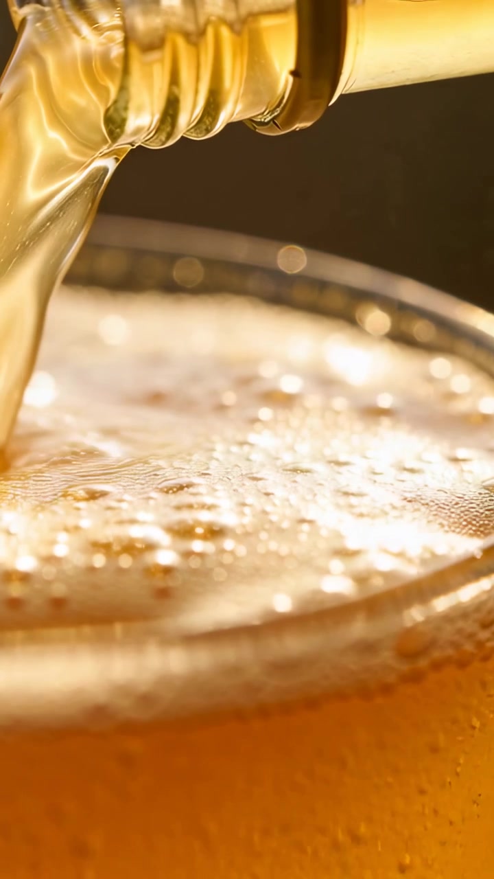 Video verticale: Inclinando il collo della bottiglia, si versa birra ambrata, riempiendo un bicchiere da pinta al bar e formando schiuma.