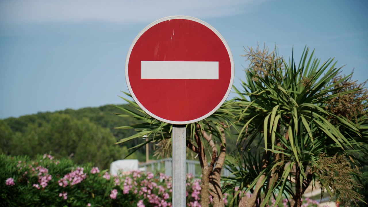 Red no entry traffic sign standing against a sunny natural background with greenery and blue sky