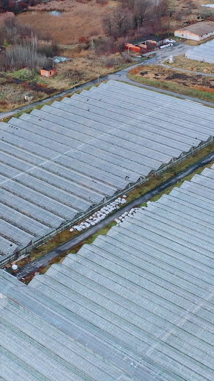 Top view of an autumn field with large glass greenhouses. Vertical video