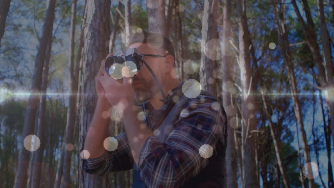 Nature photographer using film camera in sunlit pine forest, showing lens flare and circular bokeh