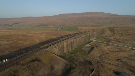 aerial drone shot pulling away from ribblehead viaduct train bridge at stunning sunrise in summer in yorkshire dales england uk with 3 peaks whernside mountain in background