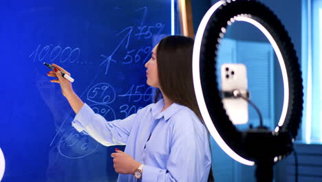fun online finance class!. a person teaches financial concepts in a bright studio, using a whiteboard and ring light to enhance video quality