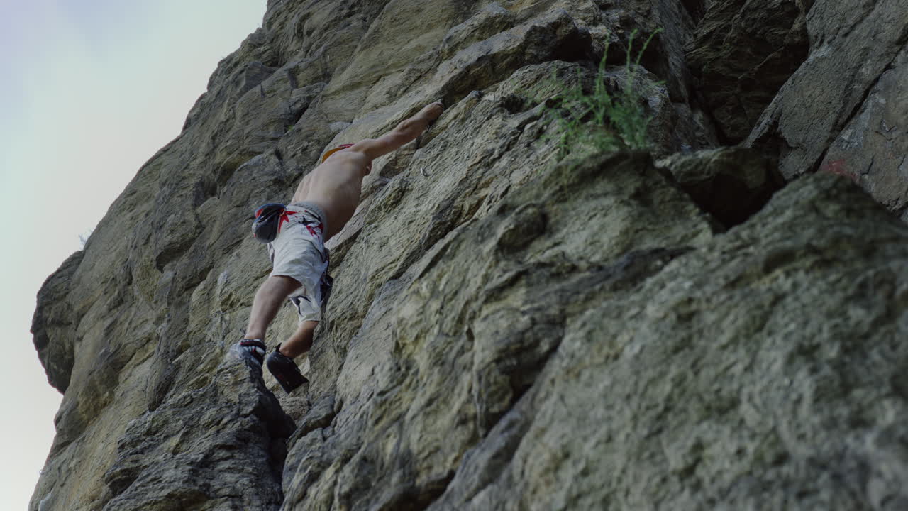 hombre con confianza sube a la roca escalada hombre en la pared de la montaña, persona rocas enormes escarpada empinada cima de la montaña sin cuerda escalada libre clima soleado pecho desnudo equipo de alpinismo, habilidades de escalada, riesgo