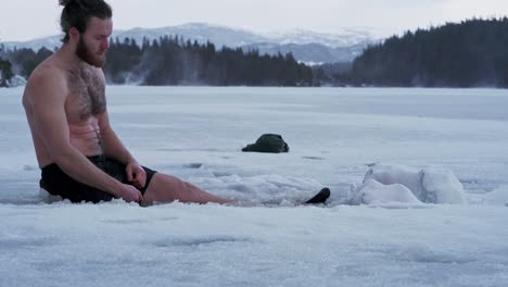 norwegian guy half naked soaking his legs on frosted lake during daytime in trondheim, norway