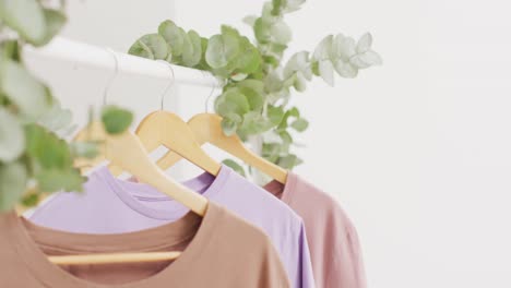 Video-of-close-up-of-beige-and-purple-t-shirts-hanging-on-white-background