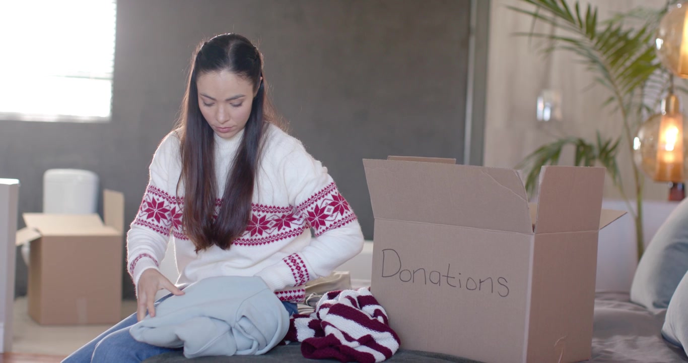 Adult woman finding donation box at home, picking up inspecting folding sweaters for Christmas