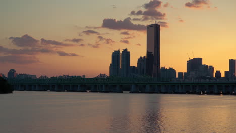 Hangang-Park-Riverfront-View-of-Silhouetted-63-Building-and-Office-Towers-in-Yeouido-District-and-Subway-Train-Moving-on-Railway-Bridge