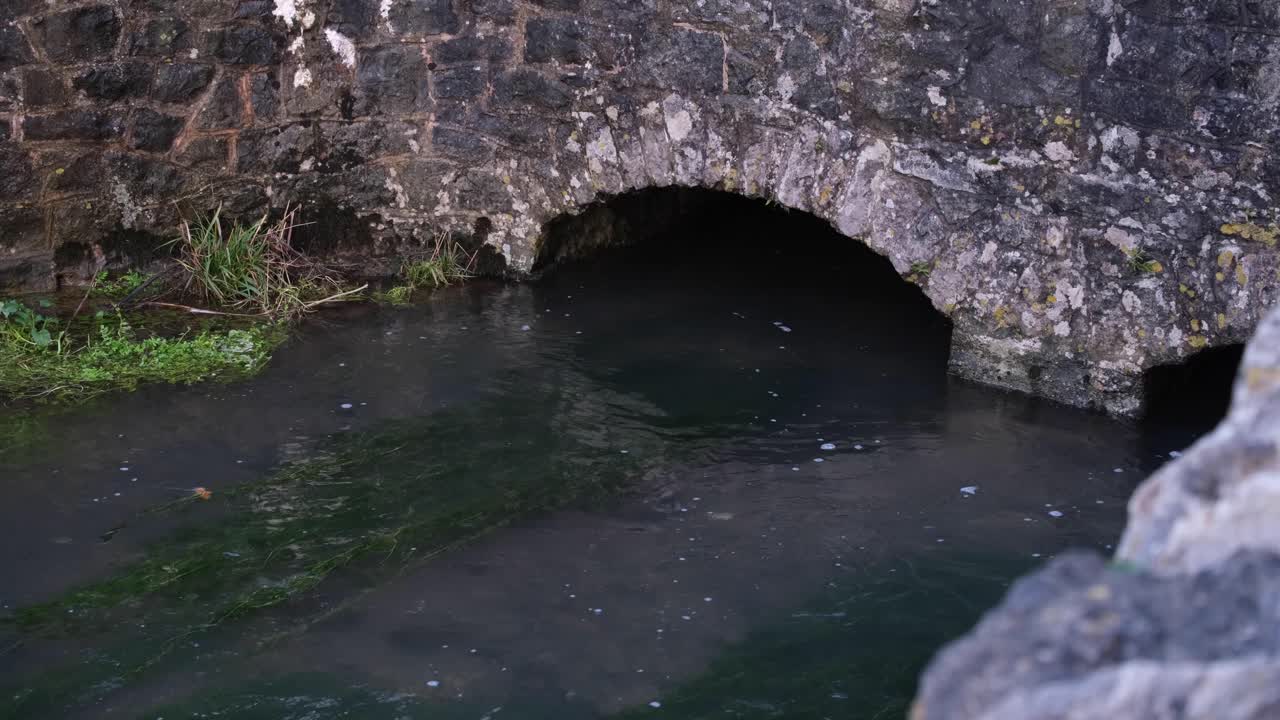 목가적이고 얕은 물이 흐르는 강은 영국 시골 체다 협곡, 서머셋, 영국 시골 마을에 있는 오래된 석조 아치 다리 아래로 흐르고 있습니다.