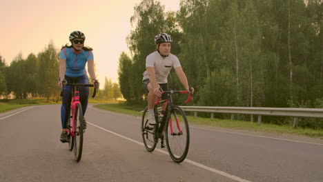 Leerer-Raum.-Sportliche-Freunde-Auf-Dem-Fahrrad-Bei-Sonnenuntergang.-Radfahrerpaar-Fährt-Die-Küste-Entlang.-Sport-Im-Naturhintergrund.-Gruppe-Von-Leuten,-Zwei-Rennradfahrer-Bei-Sonnenuntergang.