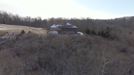 imágenes aéreas de drones que se desplazan hacia un albergue abandonado en una colina durante el invierno