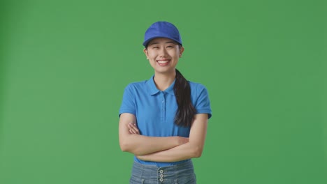 mensajera asiática en uniforme azul sonriendo cruzando los brazos en el fondo de la pantalla verde en el estudio