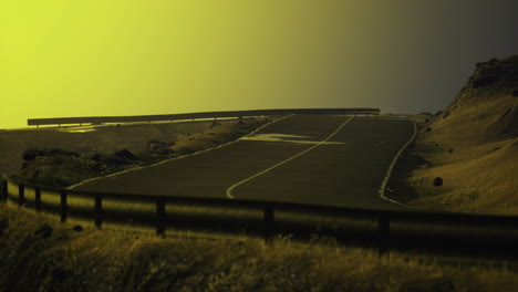 scenic winding road through grassy hills with a golden sky at sunset