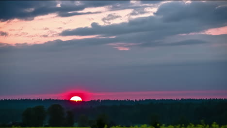 pink sunset as the sun dips below the forest on the horizon during a dramatic cloudscape - time lapse