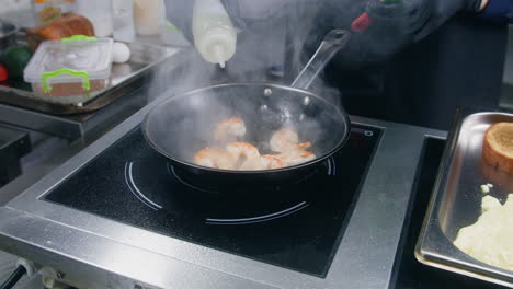 male cook fries and stirs shrimp in frying pan