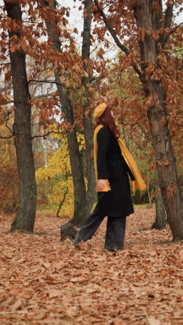 vista lateral de una dama en el bosque, esparciendo alegremente follaje seco a su alrededor, con un abrigo largo, zapatos de lona y vaqueros negros, capturando la esencia del otoño