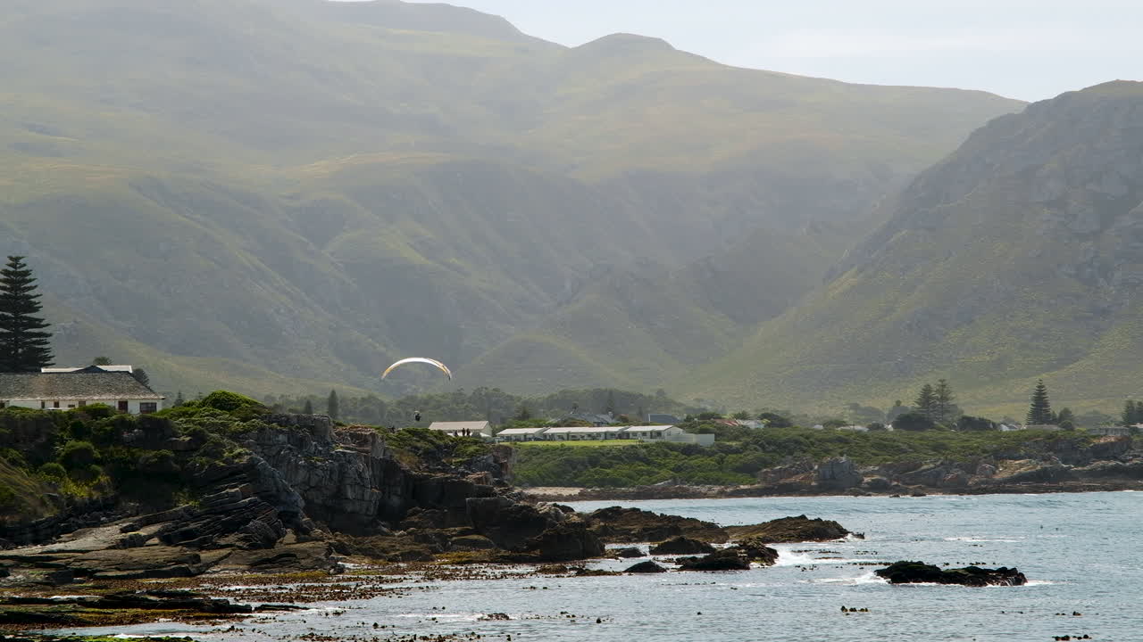 параплан летит низко над живописным побережьем, на фоне гор