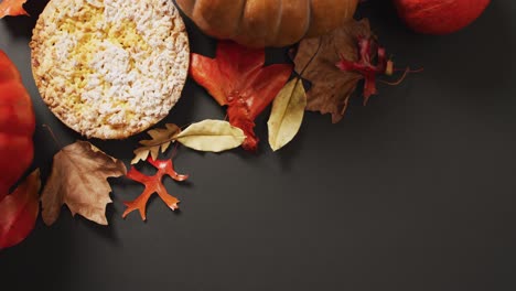 Video-of-autumn-leaves,-pumpkin-and-pie-on-black-background