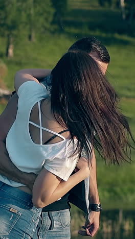 exciting long haired brunette girl in muscular man arm spins over yellow field against green trees slow motion