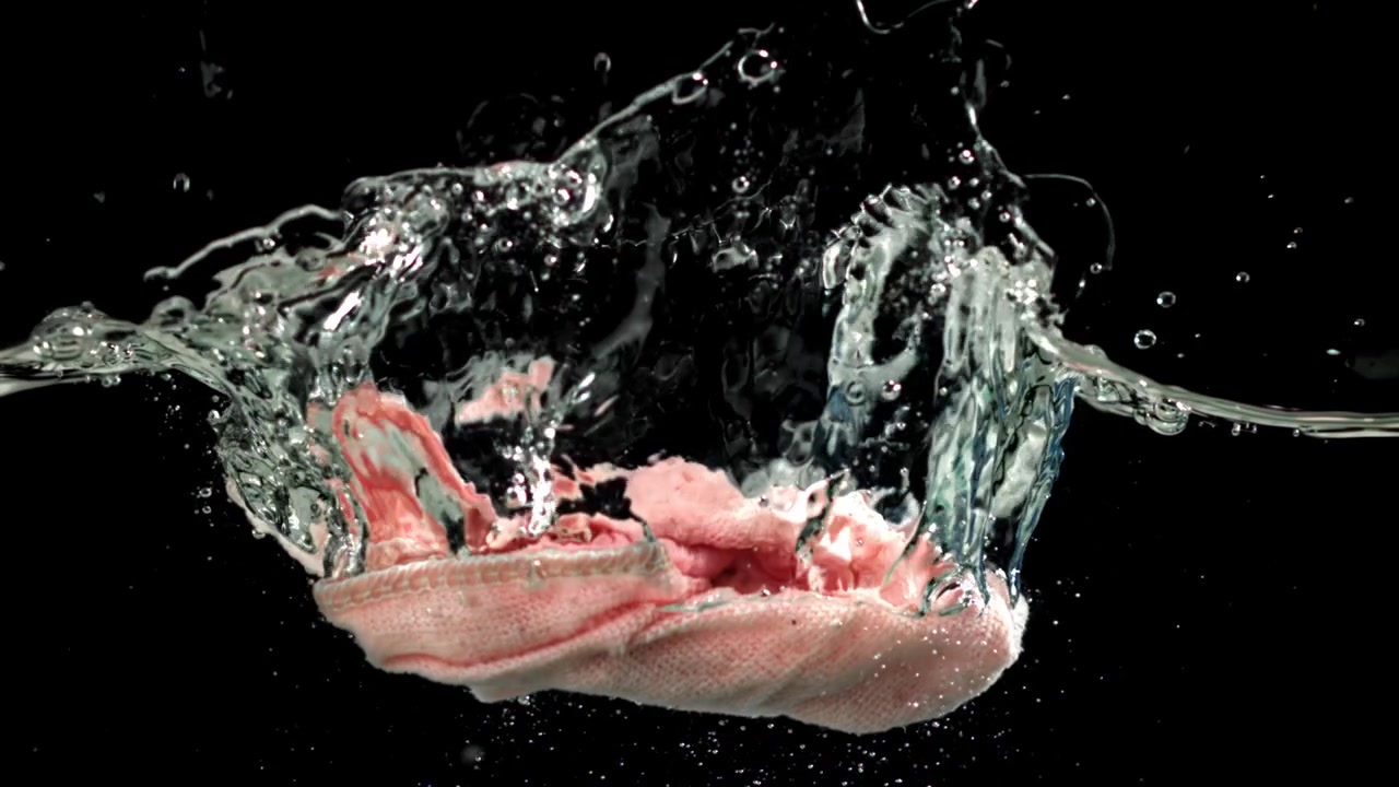 Tessuto rosa che cade nell'acqua con schizzi al rallentatore