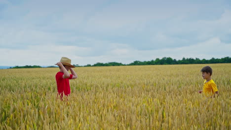 boys playing with straw hat on field. children having fun together in bright summer day. brothers throw hat on agricultural field.