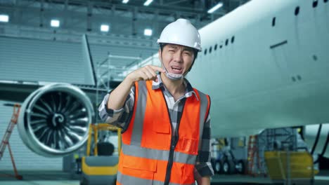 ingeniero masculino asiático con casco de seguridad de pie con aviones en el hangar. estar enojado, señalándote y gritando mientras el mantenimiento de aviones