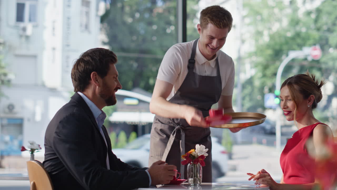 Waiter serving loving couple in restaurant. Worker bringing coffee to dating