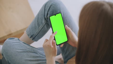 Point-of-View-of-Woman-at-Modern-Room-Sitting-on-a-Chair-Using-Phone-With-Green-Mock-up-Screen-Chroma-Key-Surfing-Internet-Watching-Content-Videos-Blogs-Tapping-on-Center-Screen