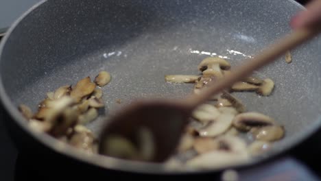 sauteing sliced mushrooms in a skillet with small amount of cooking oil - close up