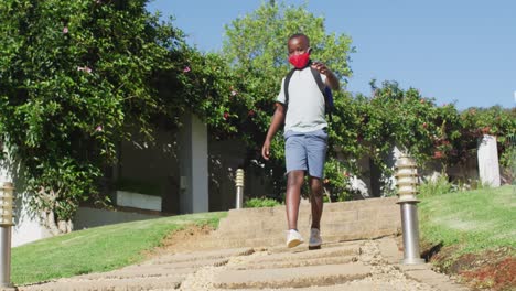 portrait of african american boy wearing face mask walking down the stairs in the garden on a bright