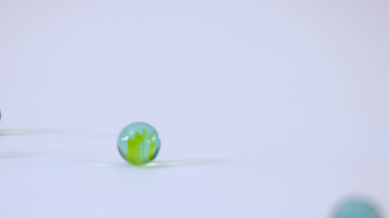 Slow motion studio shot of vibrant glass marbles dropping and rolling across white background
