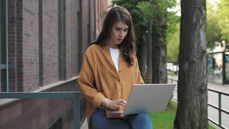 Camera-zoom-out-on-caucasian-and-african-american-students-talking-while-drinking-coffee-and-using-the-laptop-sitting-in-the-street-near-the-college