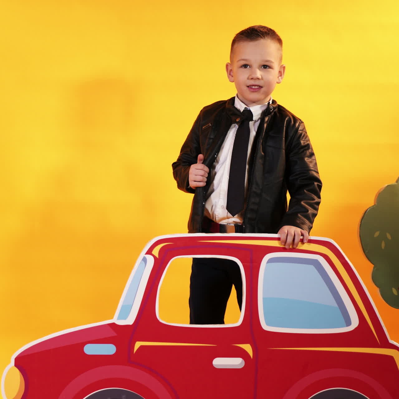 Anak laki-laki kecil dengan mobil merah cerah dengan latar belakang kuning di studio. Anak-anak bahagia. Video persegi.