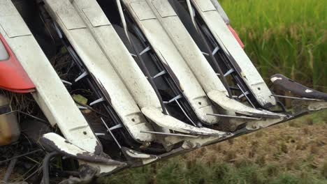 Close-up-details-of-the-multifunctional-machine-rice-harvester-tractor-driving-across-cultivated-rice-paddy-field,-farmer-harvesting-crops-reaping,-threshing,-and-winnowing