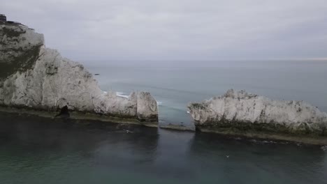 vuelo de drones aéreos de 4k 30fps junto a los acantilados blancos de las agujas en la isla de wight que muestra un faro rojo y blanco y olas rompiendo contra las rocas