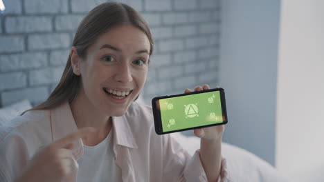 portrait of a pretty young woman showing a smartphone with mockup green screen