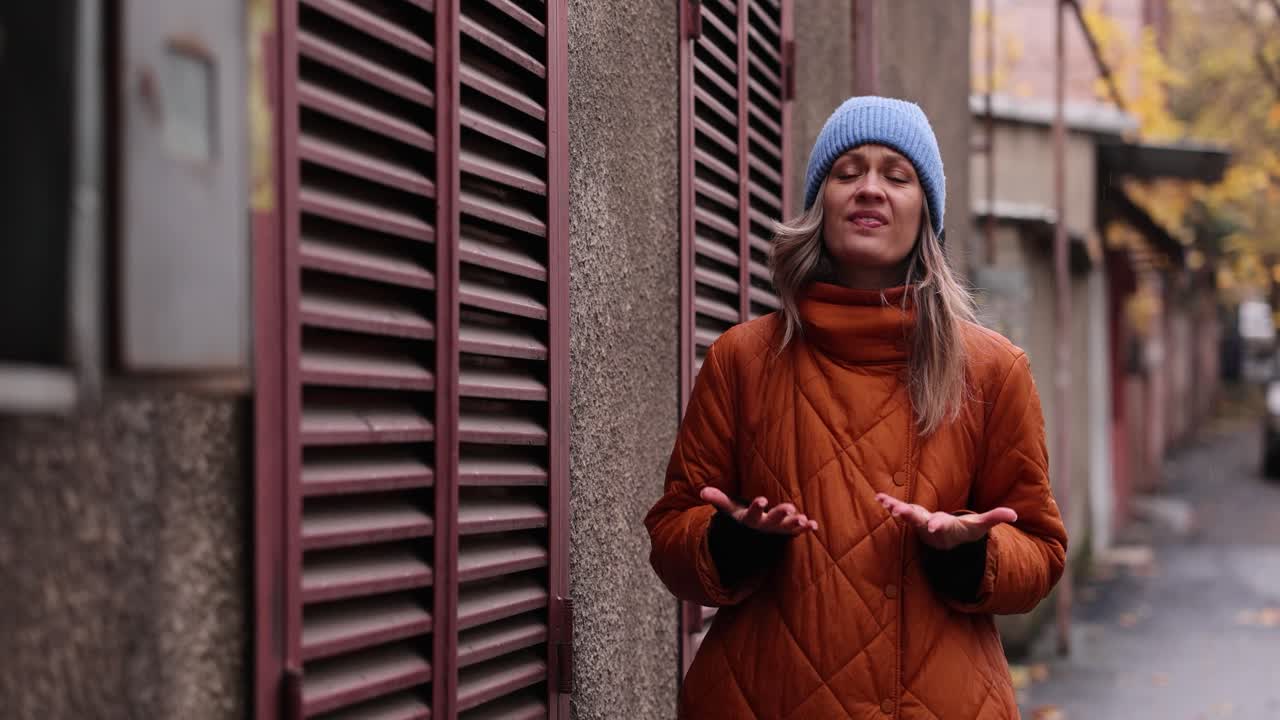 Woman in orange coat and blue hat on urban street