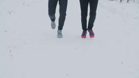 Positive-beautiful-young-healthy-couple-running-with-sportswear-through-the-forest-in-the-sunny-winter-morning.