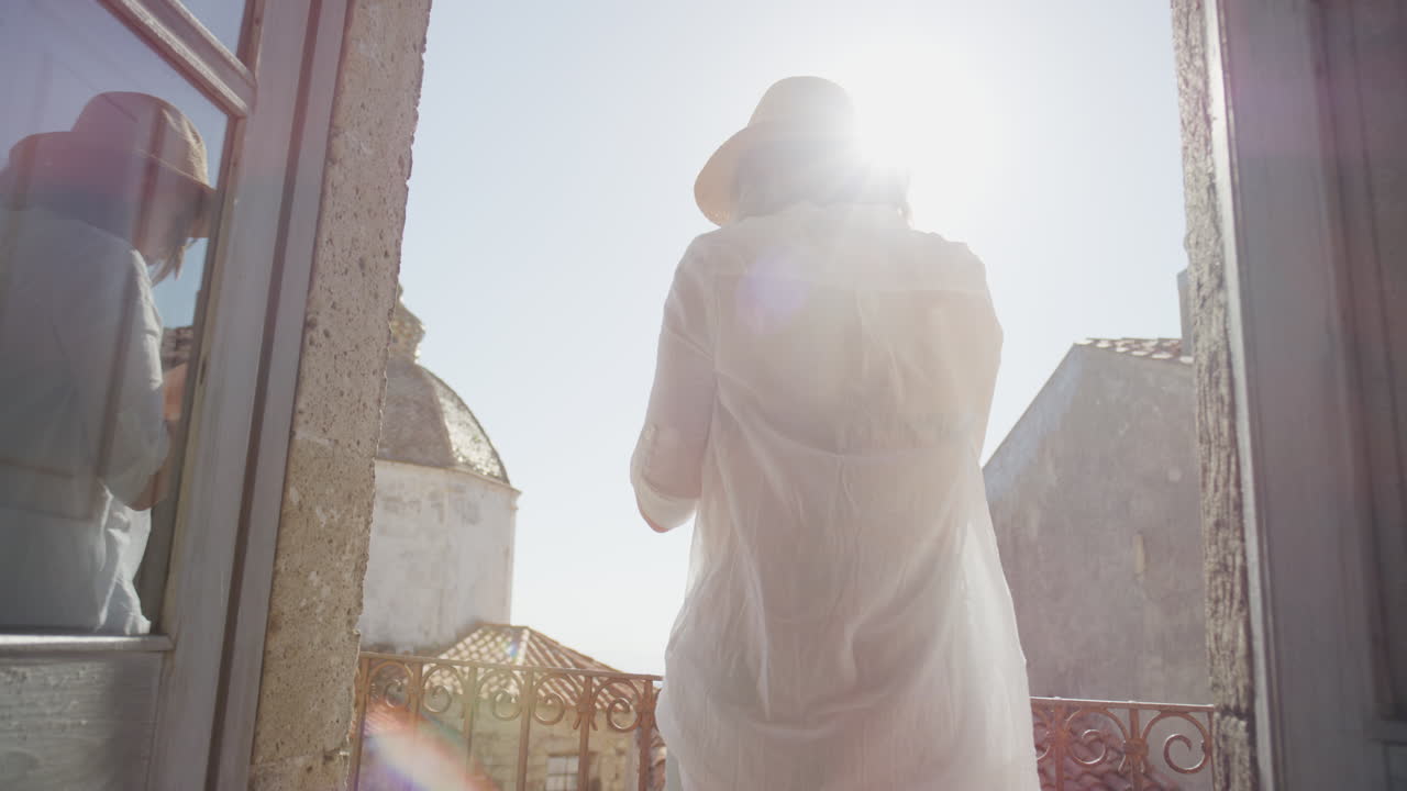 스마트폰을 사용하는 행복한 여성 사진을 찍고 여름 휴가 여행 경험을 공유하는 즐거움을 느끼고 발코니에서 아름다운 경치를 사진으로 찍고 모자를 입고 있습니다.