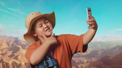 asian boy with a hat and binoculars taking a selfie on smartphone while traveling at the top of mountain. boy researcher examines something, travel tourism adventure, close up
