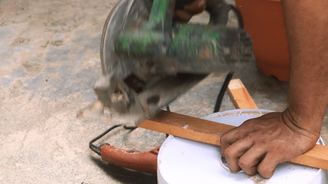 Professiobal carpenter splits with an industrial circular saw machine a small thin piece of wood to manufacture forniture in his outdoor traditional workshop small business