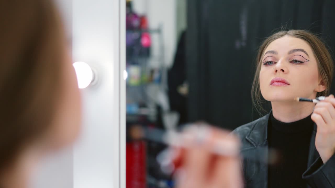 Young woman applying makeup in front of a mirror