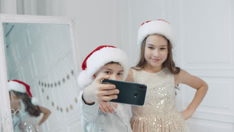 portrait of smiling children making selfie in santa hats near christmas tree.