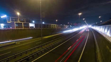 Nachtstädtisches-Zeitraffervideo-Einer-Stark-Befahrenen-Autobahn-Bei-Nacht-In-Der-Stadt,-Weiße-Und-Rote-Stadtbahnen,-Die-Von-Vorbeifahrenden-Autos-Hinterlassen-Werden