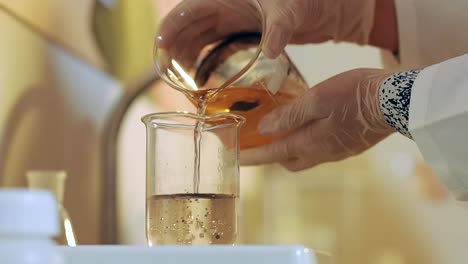 manos enguantadas vertiendo líquido en un vaso de laboratorio