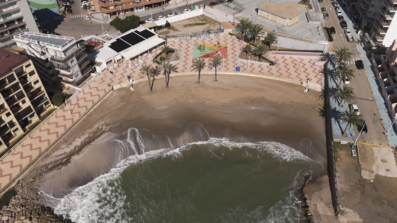 Waves lap rocks at base of seaside walkway near residential buildings