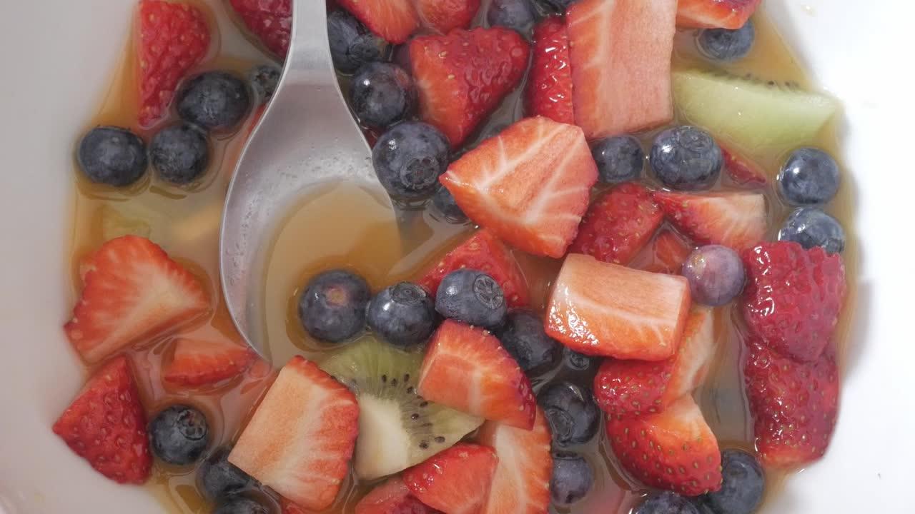 Overhead shot of colorful fruit salad with blueberries, strawberries and kiwi submerged in juice