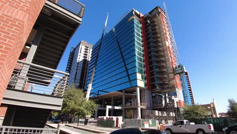 A-busy-construction-site-of-a-crane,-elevator,-workers,-and-traffic-prepares-a-new-glass-and-steel-highrise-to-join-the-Tempe,-Arizona-skyline