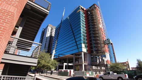 un sitio de construcción ocupado de una grúa, ascensor, trabajadores y tráfico prepara un nuevo rascacielos de vidrio y acero para unirse al horizonte de tempe, arizona
