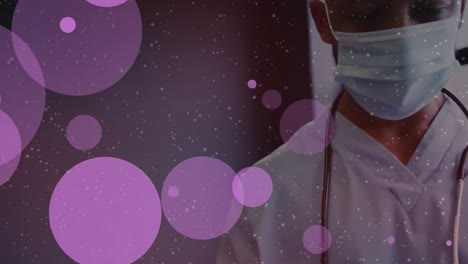 Animation-of-pink-dots-over-caucasian-male-doctor-in-face-mask