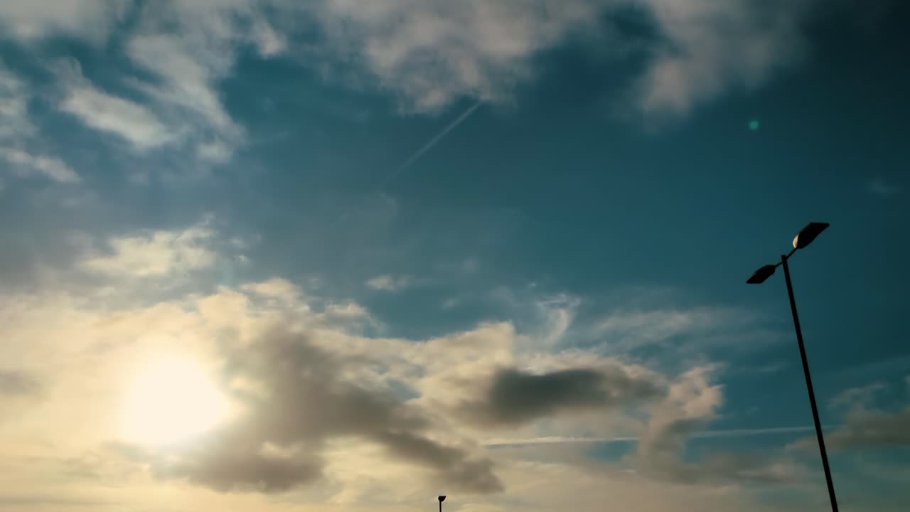 Timelapse of Sun Rays in Early Morning with Fluffy Clouds Passing By Quickly with Lone Street Lamp and Rich Blue Sky Background 4K